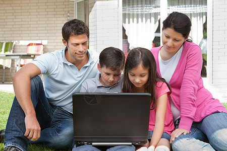 使用膝上型电脑在后院的年轻家庭图片