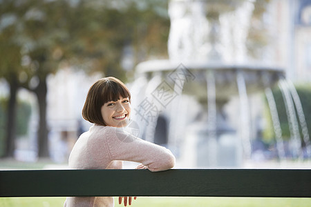 坐在模糊喷泉前的长椅上 一个微笑着的年轻女人的侧面肖像图片
