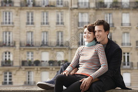 微笑的年轻夫妇坐在联排别墅前的桥上图片