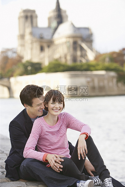 在圣母教堂前 坐在河岸的一对幸福快乐的情侣图片