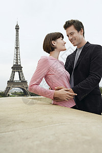 一对年轻夫妇与埃菲尔铁塔在远处相拥的侧面视图图片