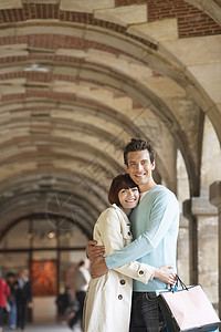 一对夫妇的侧视角 夹在拱门下面的购物袋购物微笑休息日幸福成人游客建筑学娱乐感情团结图片