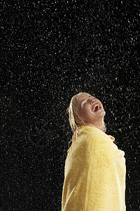 一个笑着的年轻女人的侧面 被雨中裹在黄毛巾上图片