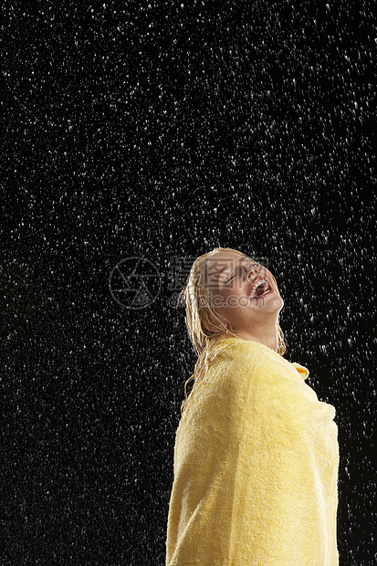 一个笑着的年轻女人的侧面 被雨中裹在黄毛巾上图片