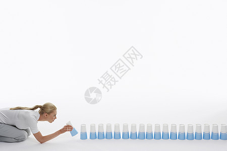 一个年轻女性的侧面景象 将塑料杯挂在地板上 在白色背景下图片