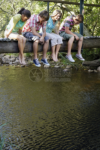 坐在木桥上看着溪流的十几岁的男孩女孩们快乐图片