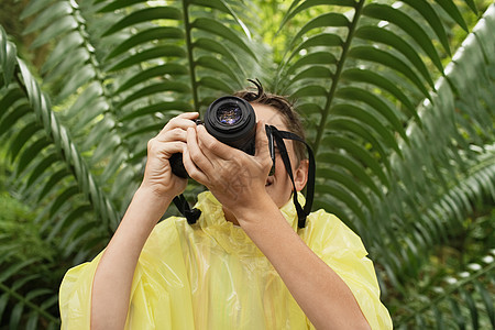 穿雨衣的年轻男孩在实地考察期间 在森林里拍照青春期勘探好奇心蕨类森林树叶教育生命专注男性图片