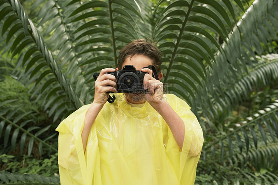 穿雨衣的年轻男孩在实地考察期间 在森林里拍照好奇心教育旅行植物树叶相机男性娱乐摄影叶子图片