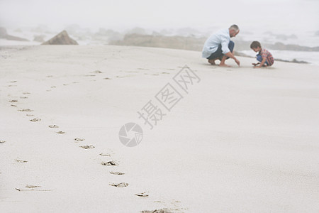 父亲和儿子在海滩玩沙子的侧景色图片