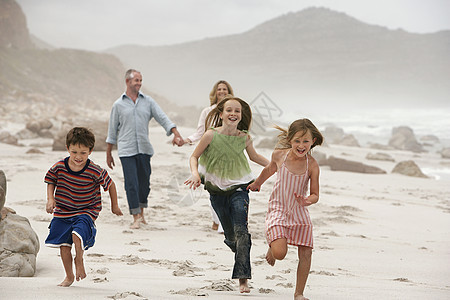 快乐的孩子在海滩上奔跑 父母在背景中行走图片