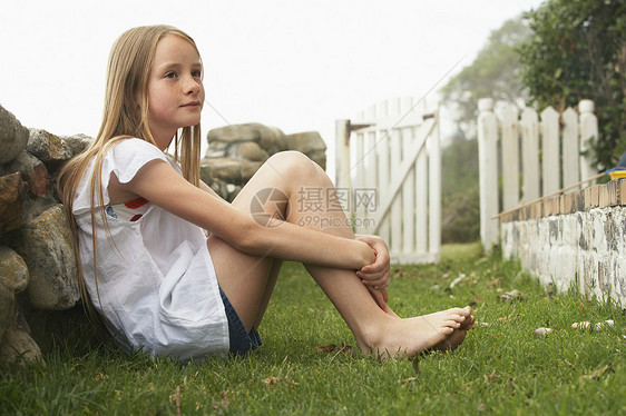 小女孩坐在院子旁仰靠石墙的侧面视图图片