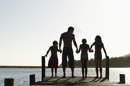 三个孩子手牵着手站在码头边的父亲的后视图图片