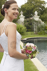 美丽的年轻新娘在泳池边拿着花束图片