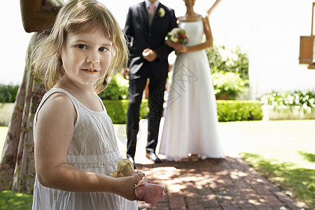 一个可爱女孩的肖像 拿着花瓣 新娘和新郎站在背景上图片