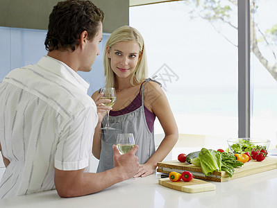 在厨房柜台拿着葡萄酒杯的年轻夫妇图片