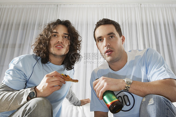 两个认真的年轻人在看电视 喝着啤酒吃披萨图片