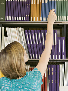 一位年轻女性从图书馆书架上取书的近视图片