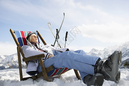 在雪山的甲板椅上躺着的女人的侧视角图片