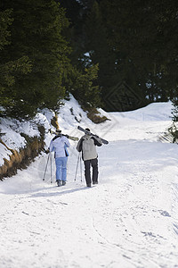 滑雪夫妇在滑雪山坡下行走 肩膀背靠后搭起滑雪车图片