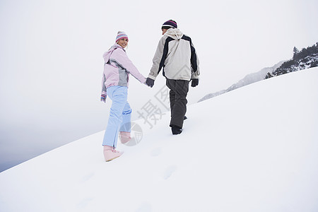 一对在雪覆盖的山丘上行走的夫妇 后仰低角视图成人服装眼神女士夫妻休闲两个人男子团结中年图片