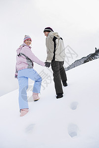 一对在雪覆盖的山丘上行走的夫妇 后仰低角视图微笑两个人成人团结活动女性快乐滑雪服夫妻女士图片