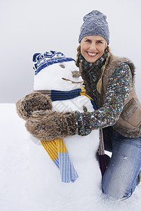 带着雪人在雪花覆盖的山丘上拥抱雪人微笑的年轻女子图片
