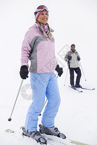 妇女滑雪员站在滑雪斜坡上 男子站在背景滑雪上图片