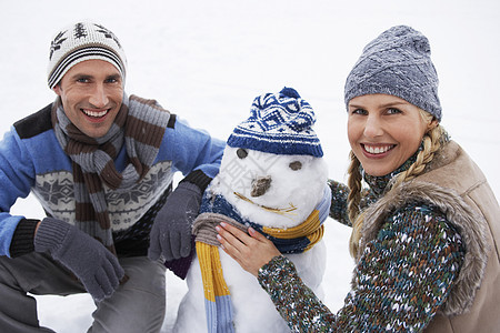 快乐的一对年轻夫妇在雪上山上跪着和穿雪衣雪人图片