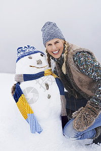 快乐的年轻女子 在雪地上跪在雪人脚下图片
