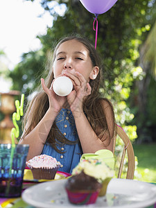 在户外生日派对上吹气球的年轻女孩图片