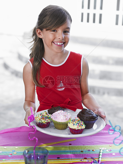 一个带着纸杯蛋糕盘微笑的小女孩的肖像图片