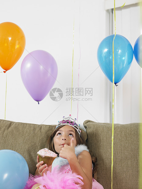 年轻女孩坐在沙发上 仰望着有纸杯蛋糕的气球图片
