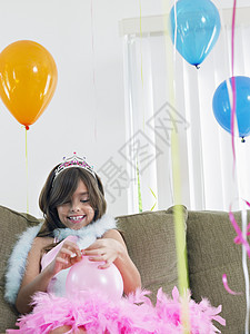 在沙发上微笑的年轻女孩 准备生日气球孩子长椅蟒蛇闲暇庆典房间专注童年羽毛快乐图片
