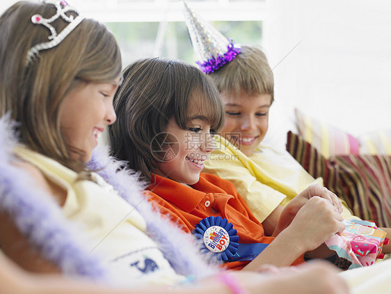 三个孩子在生日派对上坐在沙发上 一个打开礼物图片