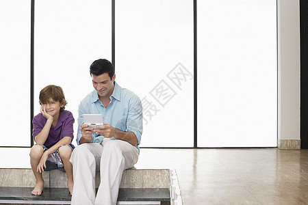 快乐的父亲玩手持电子游戏 坐在家里儿子旁边图片