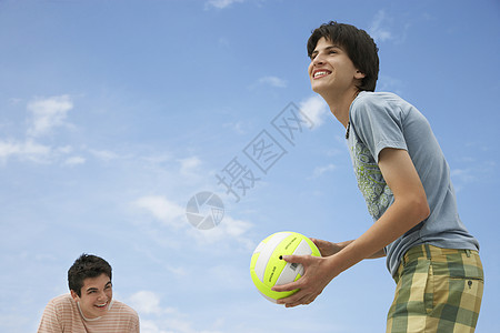 快乐的少年男孩玩海滩排球对抗天空的低角度视角图片