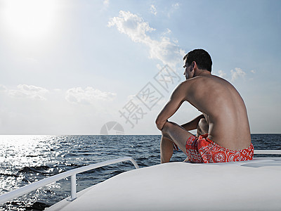 坐在游艇边缘观海的年轻男子的近视图片
