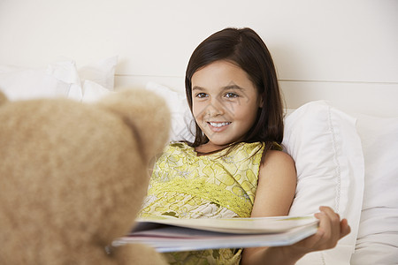 快乐女孩在床上给泰迪熊读故事书阅读就寝玩具熊孩子房子幸福故事微笑友谊时间图片