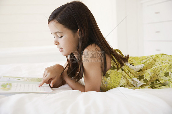 小女孩在床上阅读故事书的侧面视图图片