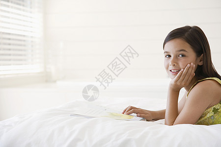床上写着故事书的放松小女孩的肖像图片