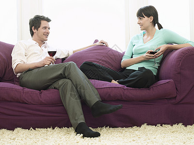 快乐的一对年轻夫妇 带着葡萄酒杯 在沙发上放松图片