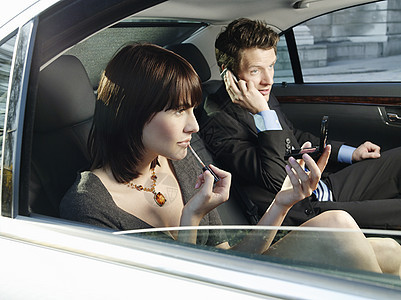 在汽车后座的两对夫妇 女性申请化妝男子使用手机享受唇彩两个人女士财富学徒镜子商务头发电话图片