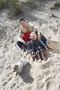 在沙沙滩上放松狗的快乐家庭三人全长肖像图片