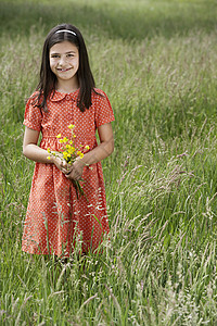 快乐的年轻女孩在草地上拿着鲜花的肖像图片