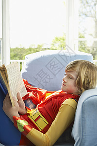 一个穿着超人服装的男孩的侧边景 阅读书在室内图片