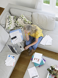 在沙发上携带财务文件使用笔记本电脑的成年妇女高视率图片