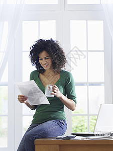 年轻的非裔美国妇女阅读文件 桌上有一个咖啡杯的咖啡杯图片