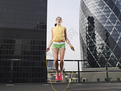一位年轻女子跳过伦敦市中心大楼的低角度观景图片