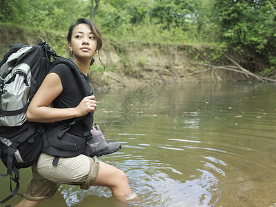 一位年轻混合种族妇女在森林水中行走时背背背背背背包的侧面景象图片