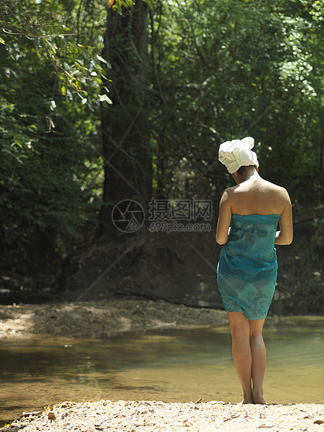 站在森林湖边头部和身体上裹着毛巾的妇女的后视镜图片